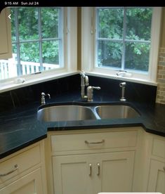 a black counter top in a kitchen with white cupboards and drawers next to two windows