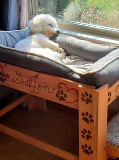 a white dog laying on top of a wooden bed in front of a large window