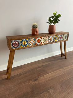 two potted plants sit on top of a wooden bench with colorful tile designs painted on it