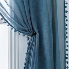 a blue curtain with pom - poms hanging from it's side in front of a window