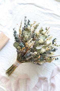 a bouquet of dried flowers sitting on top of a white cloth covered tablecloth next to a book