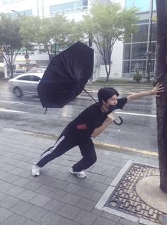 a man holding an umbrella on the side of a road next to a tree in the rain