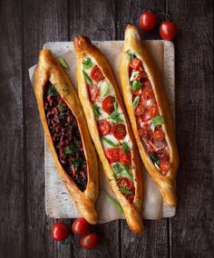 two long breads with tomatoes and other toppings are on a cutting board next to cherry tomatoes