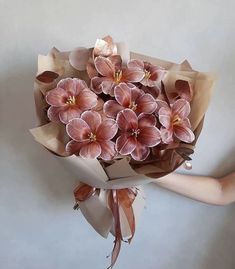 a person holding a bouquet of flowers with brown paper wrapped around the stems and petals