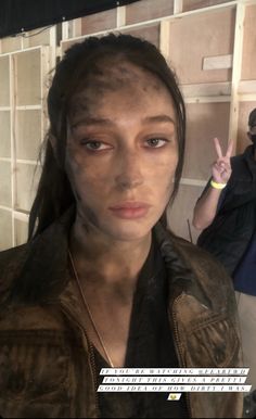 a woman with mud on her face standing in front of a man holding up his peace sign