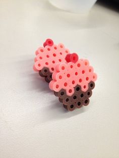 two pink and brown earrings sitting on top of a white table next to a cup