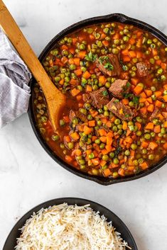 two bowls filled with stew and rice on top of a white counter next to a wooden spoon