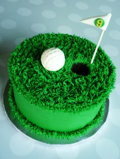 a green cake with a golf ball and flag on the top that is made to look like grass