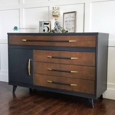 a black and brown dresser sitting on top of a hard wood floor next to a white wall