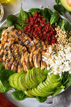 a white plate topped with chicken, rice and spinach next to sliced avocado