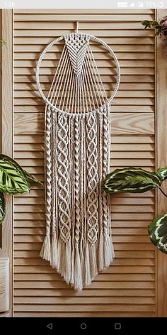 a macrame hanging on the wall next to some plants