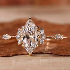 an engagement ring with a pear shaped diamond surrounded by small diamonds on top of a leaf