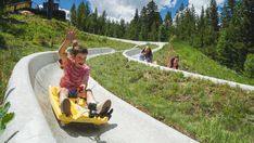 a young boy riding on a yellow bumper car down a hill with other people in the background