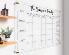 a wall mounted calendar on a whiteboard with wooden shelves and potted plants next to it