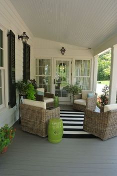 a porch with wicker furniture and potted plants on the front steps, along with black and white striped rugs