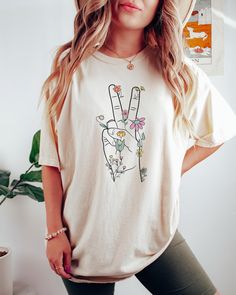 Looking for a shirt that will show your support for peace and love? Look no further than the peace sign shirt! This shirt is perfect for anyone who wants to express their love for peace and happiness. The shirt features a hand giving the peace sign surrounded by wildflowers making it a great choice for any fashion-savvy individual. Please not that this T-shirt is a Standard Unisex fit, if you would like an oversized look then size up 1 to 3 sizes. Comes in multiple colors! ✨️SIZE AND FIT: Your s White Hippie T-shirt For Spring, White Crew Neck Hippie Top, White Hippie Tops With Letter Print, Hippie White Short Sleeve T-shirt, Hippie Style White Short Sleeve T-shirt, White Hippie Crew Neck T-shirt, White Crew Neck Hippie T-shirt, Hippie T-shirt With Screen Print For Spring, Spring Hippie T-shirt With Screen Print