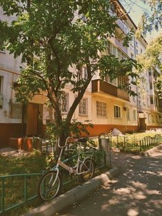 a bike parked next to a tree in front of an apartment building with balconies