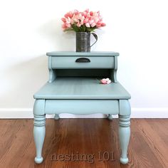 a small blue table with flowers in a vase on top and the word nesting 101 below it