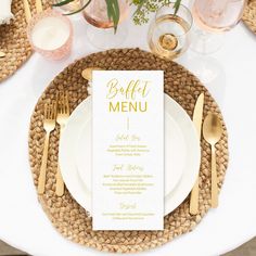 a table setting with white plates and silverware, gold cutlery and greenery