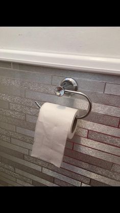 a roll of toilet paper hanging from a metal holder on a brick wall in a bathroom