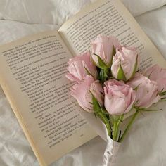 a bouquet of pink flowers sitting on top of an open book laying on a bed