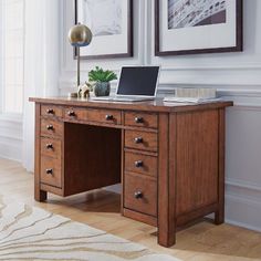 a wooden desk with a laptop on it in front of two framed pictures and a rug