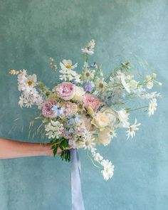 a woman holding a bouquet of flowers in her hand on a blue background with white daisies and pink roses