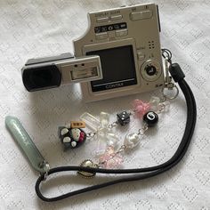 a camera and some beads on a white table cloth with a black cord attached to it