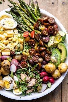 a white bowl filled with different types of vegetables on top of a wooden table next to an egg