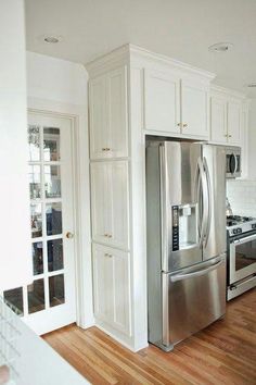 a stainless steel refrigerator in a white kitchen with wood floors and cabinets on both sides