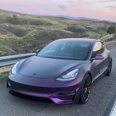 a purple sports car parked on the side of a road in front of a mountain