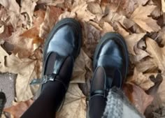 a person wearing black shoes standing on top of leaf covered ground with their feet in the air