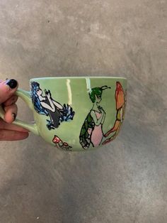 a hand holding a green coffee cup with cartoon images on it