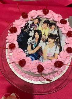 a cake with pink frosting and cherries on it, sitting on a table