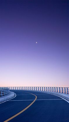 an empty road with the moon in the sky above it and a bridge on one side