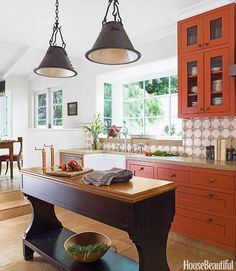 a kitchen with red cabinets and an island in front of the countertop, along with two hanging lights