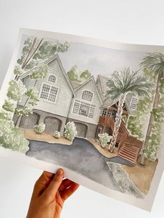 a hand holding up a watercolor painting of a house