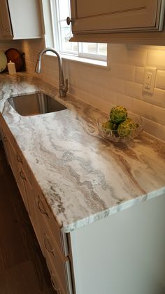 a kitchen counter top with a bowl of flowers on the sink and window in the background