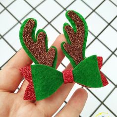 two green and red bowknots with glittery antlers on them are held in someone's hand