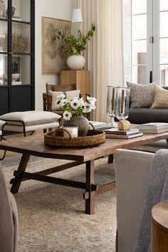 a living room filled with furniture and flowers on top of a coffee table in front of a window