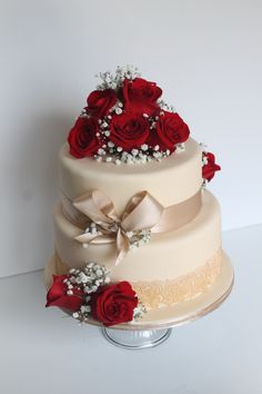 a three tiered cake with red roses and baby's breath on the side