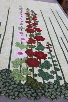 a quilted table runner with red and pink flowers in the center on top of it