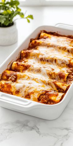 lasagna casserole in a white dish on a marble countertop next to a potted plant