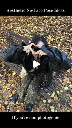 a woman sitting on top of a park bench in the fall with her hands to her face