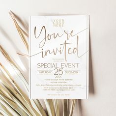 a white and gold wedding party card with palm fronds next to it on a table