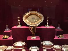 a display case with many different types of silver and gold dishes on red stands in front of a purple wall