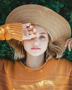 a woman wearing a brown hat and sweater is posing for the camera with her hands on her head