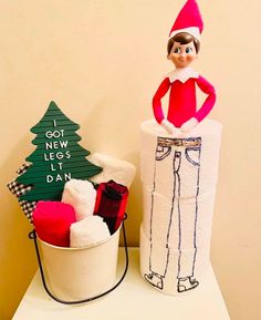 an elf is sitting on top of a toilet paper roll next to a christmas tree