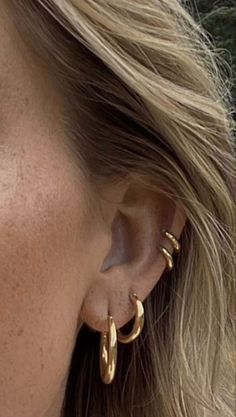 a close up of a person wearing large gold hoop earrings on their ear and nose