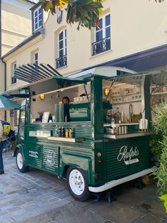 a green food truck parked in front of a building with an awning over it